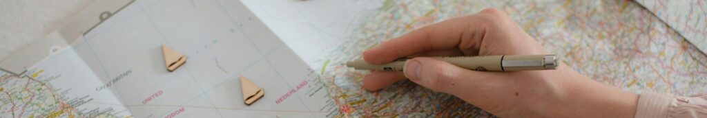 Hand holding pen over Europe map, planning travel route with markers.