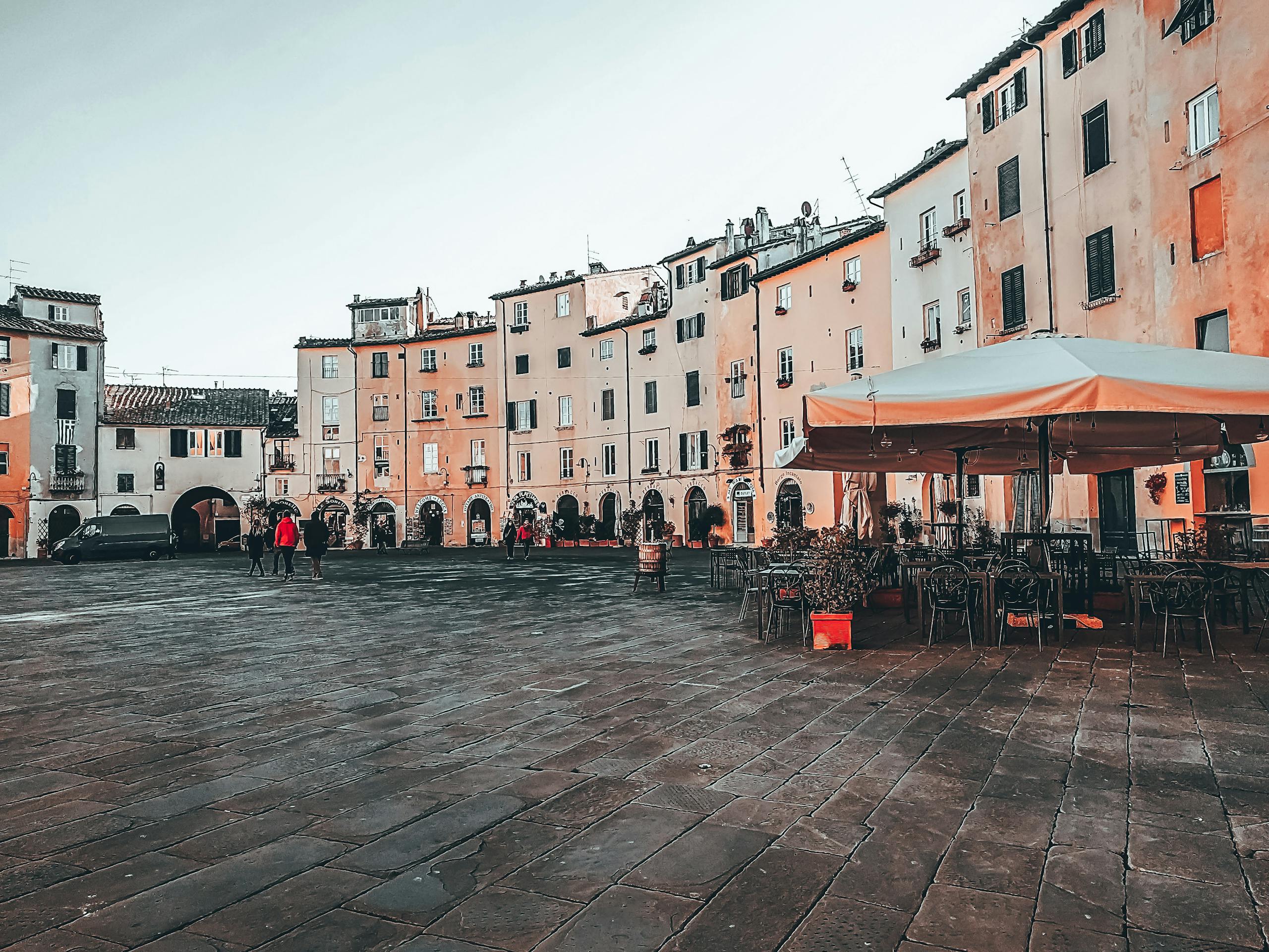 Light blue cloudless sky above people and outdoors cafe on paved square in daytime